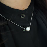 A dainty pearl pendant necklace with a silver chain on a person wearing a black top.