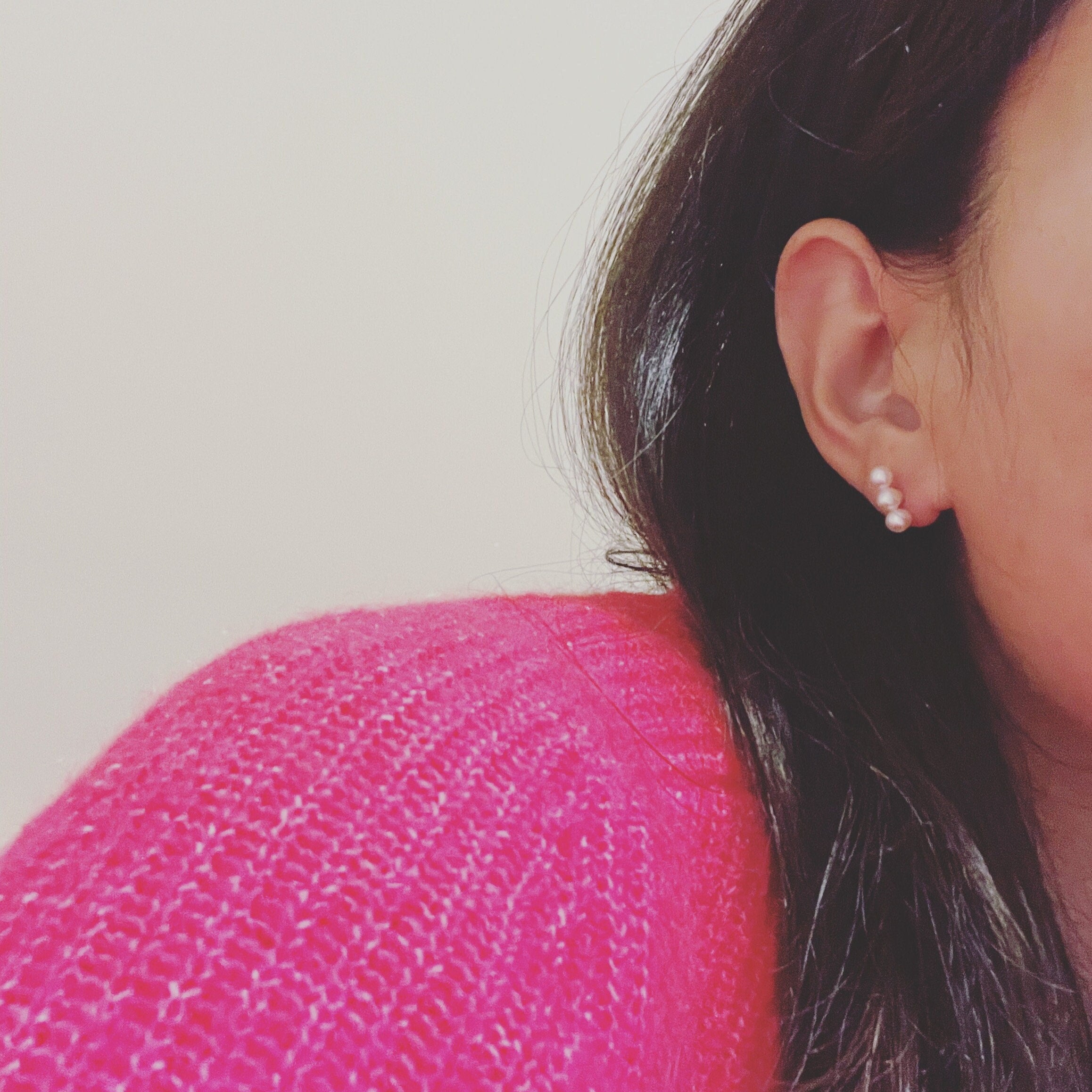 A woman wears three bead freshwater pearl earrings with a pink sweater.