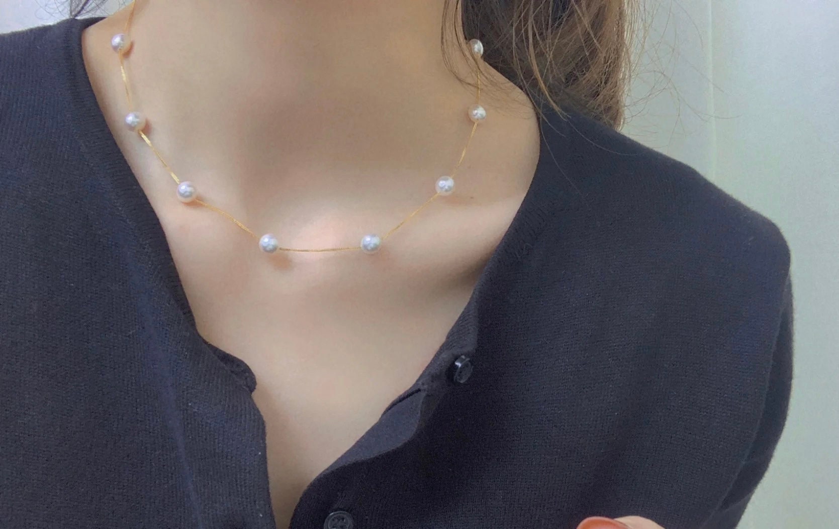 Dainty pearl necklace with a 14K gold plated chain on a person wearing a black top.