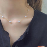 Dainty pearl necklace with a 14K gold plated chain on a person wearing a black top.