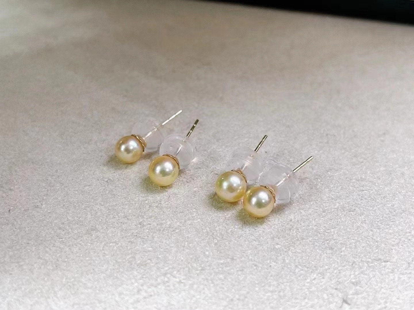 Four golden freshwater pearl stud earrings are displayed on a light gray surface.