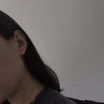 A woman wears a single pearl stud earring and a gold chain necklace.