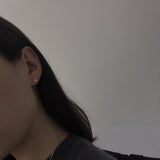 A woman wears a single pearl stud earring and a gold chain necklace.