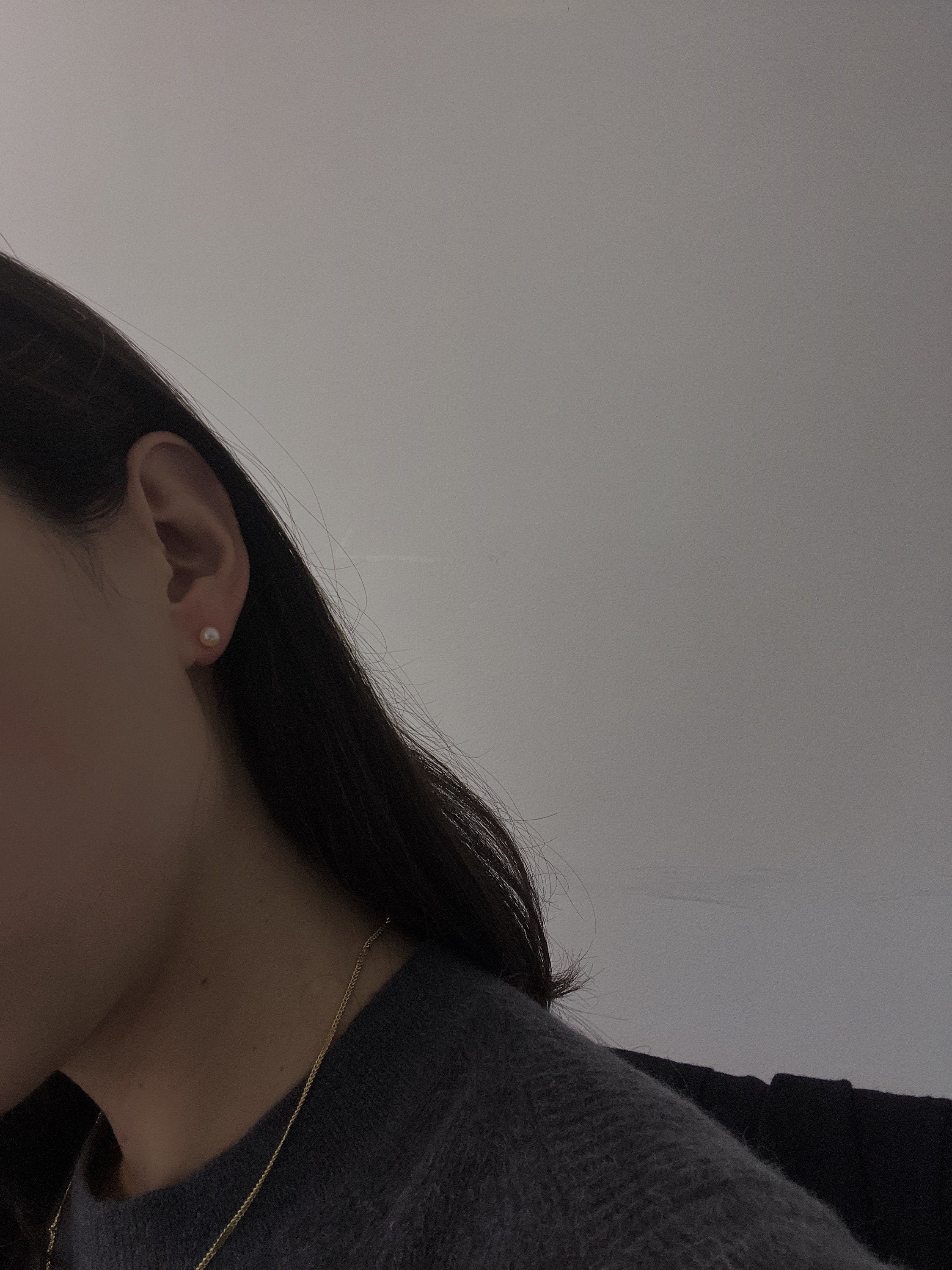 A woman wears a single pearl stud earring and a gold chain necklace.