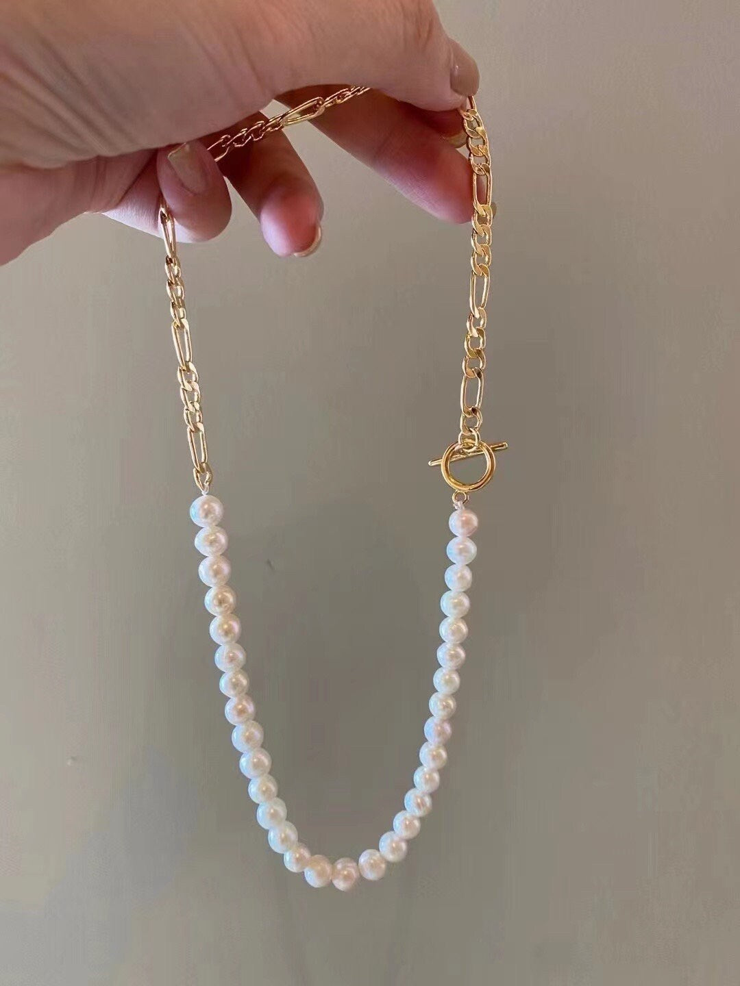 A hand holds a freshwater pearl necklace with a gold-plated chain and toggle clasp.