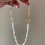 A hand holds a freshwater pearl necklace with a gold-plated chain and toggle clasp.