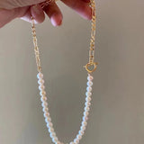 A hand holds a freshwater pearl necklace with a gold-plated chain and toggle clasp.