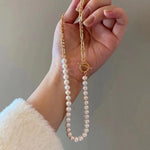 A hand holds a freshwater pearl necklace with a gold-plated chain and toggle clasp.