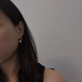 A woman wears a single hoop earring with a white pearl drop.