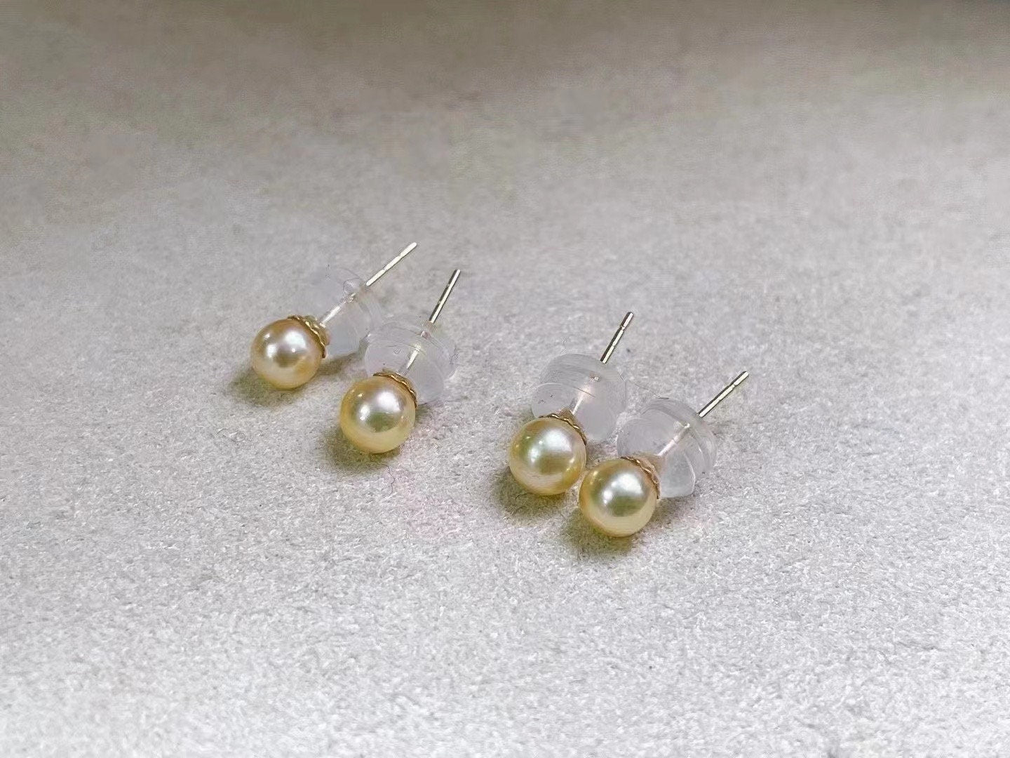Four golden freshwater pearl stud earrings with clear backings are displayed on a white surface.