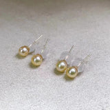 Four golden freshwater pearl stud earrings with clear backings are displayed on a white surface.