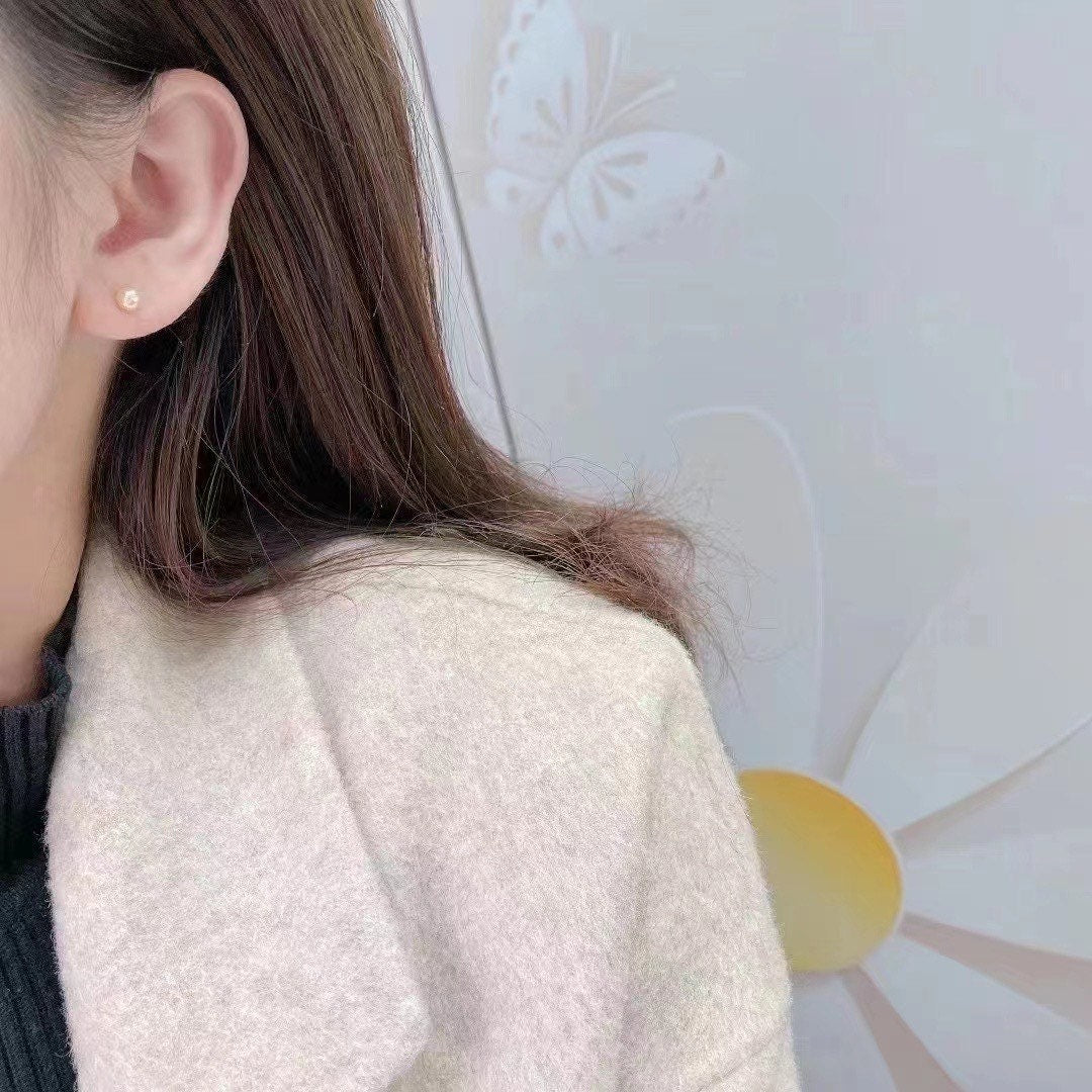 A woman wears a single golden pearl stud earring.