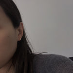 A woman wears a single pearl stud earring in her right ear.