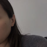 A woman wears a single pearl stud earring in her right ear.