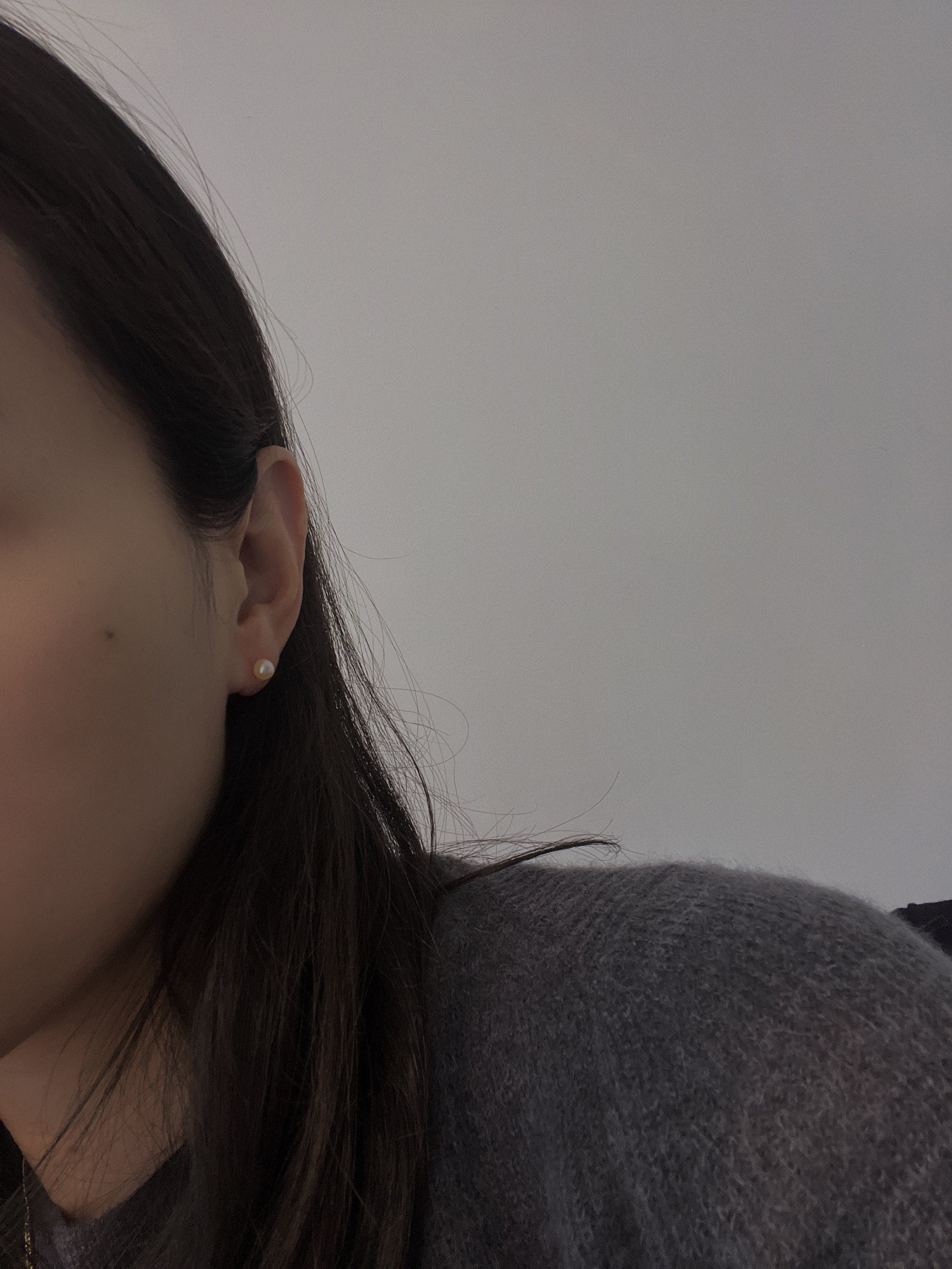 A woman wears a single pearl stud earring in her right ear.