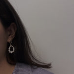 A woman wears a pearl hoop earring, showcasing its design and size.