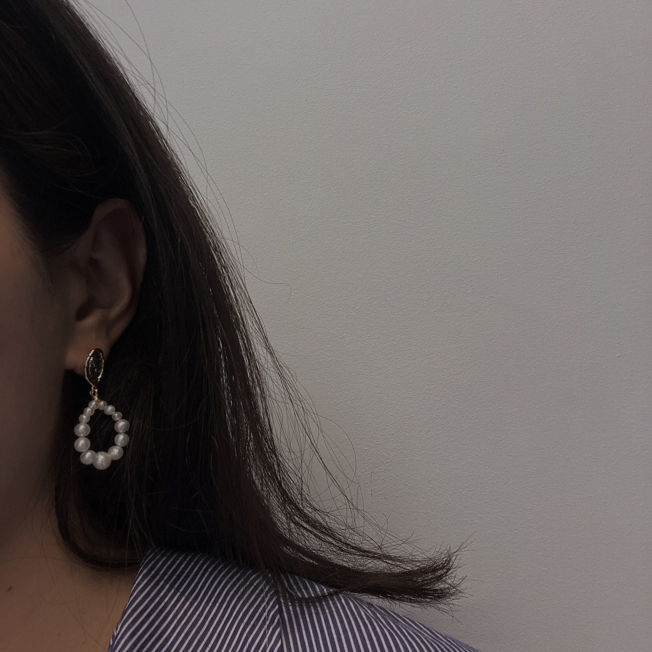 A woman wears a pearl hoop earring, showcasing its design and size.