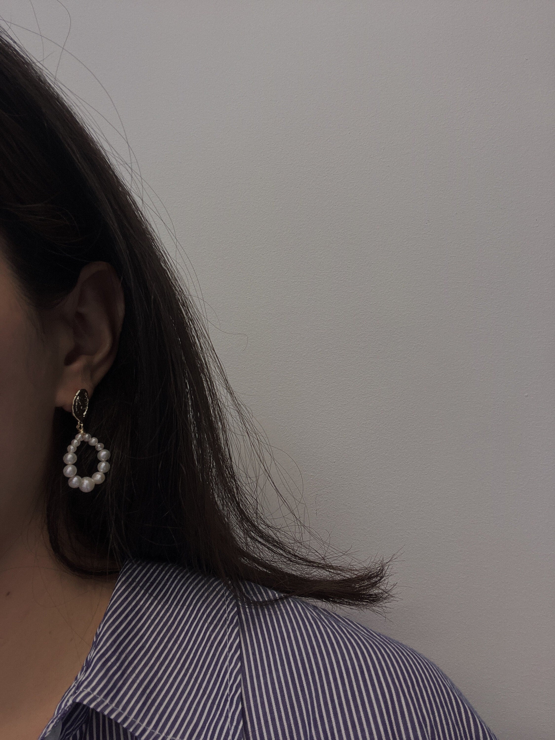 A woman wears a pearl hoop earring, showcasing its design and size.