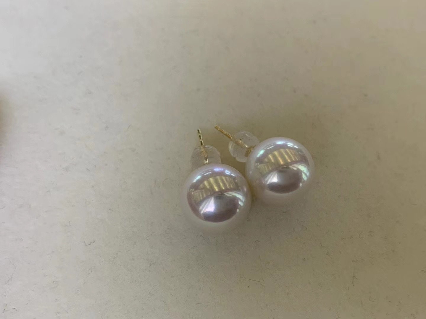 Large white pearl stud earrings with gold posts are displayed on a light surface.