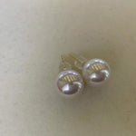 Large white pearl stud earrings with gold posts are displayed on a light surface.