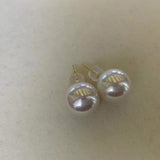 Large white pearl stud earrings with gold posts are displayed on a light surface.