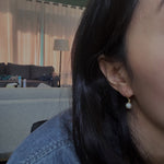 A close-up of a person wearing a single pearl hoop earring.