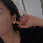 Large white pearl stud earrings on a woman's ear.