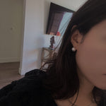 A woman wears a large, round pearl stud earring.