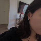 A woman wears a large, round pearl stud earring.