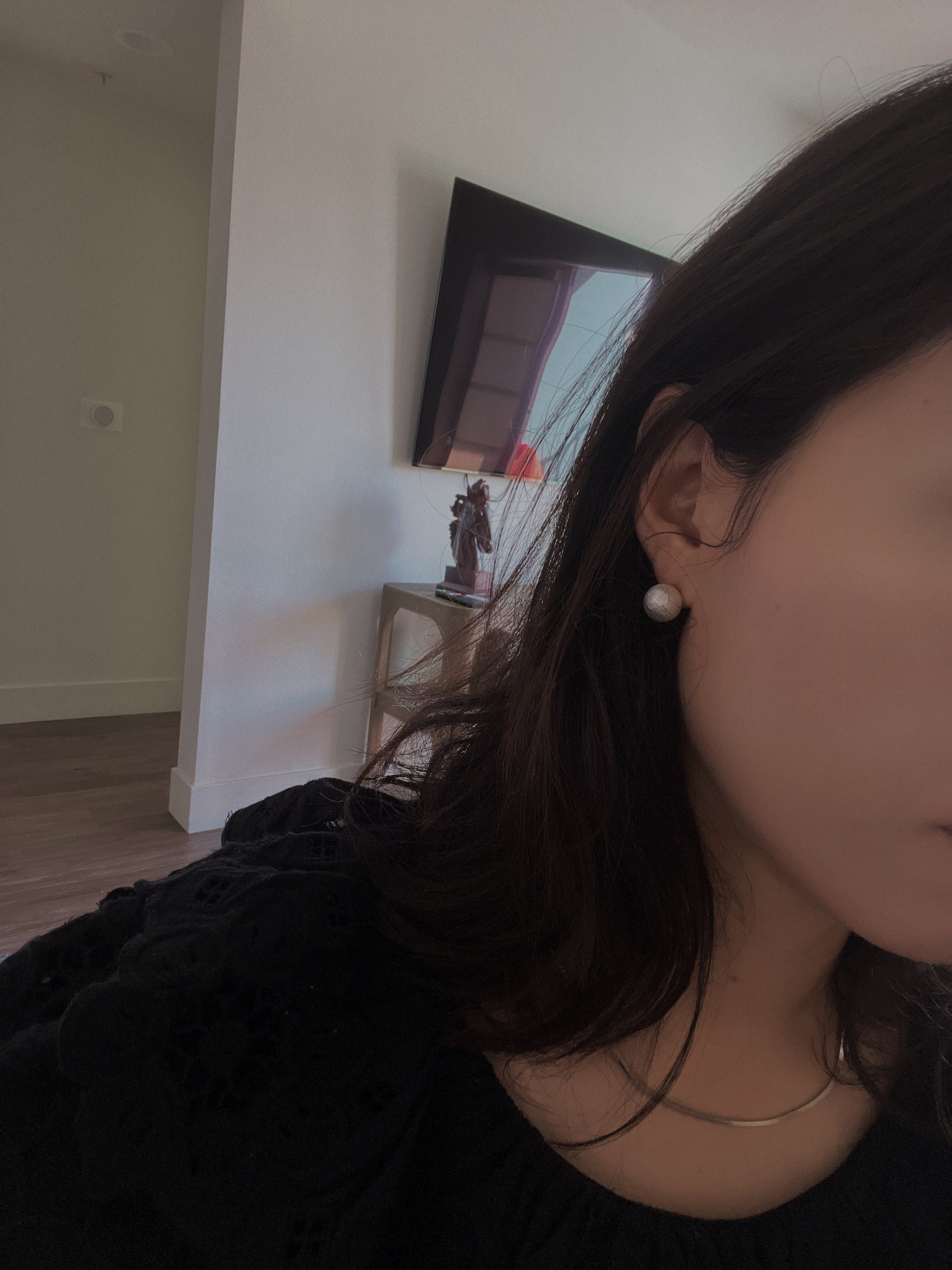 A woman wears a large, round pearl stud earring.