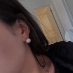 Large white pearl stud earring on a woman's ear.