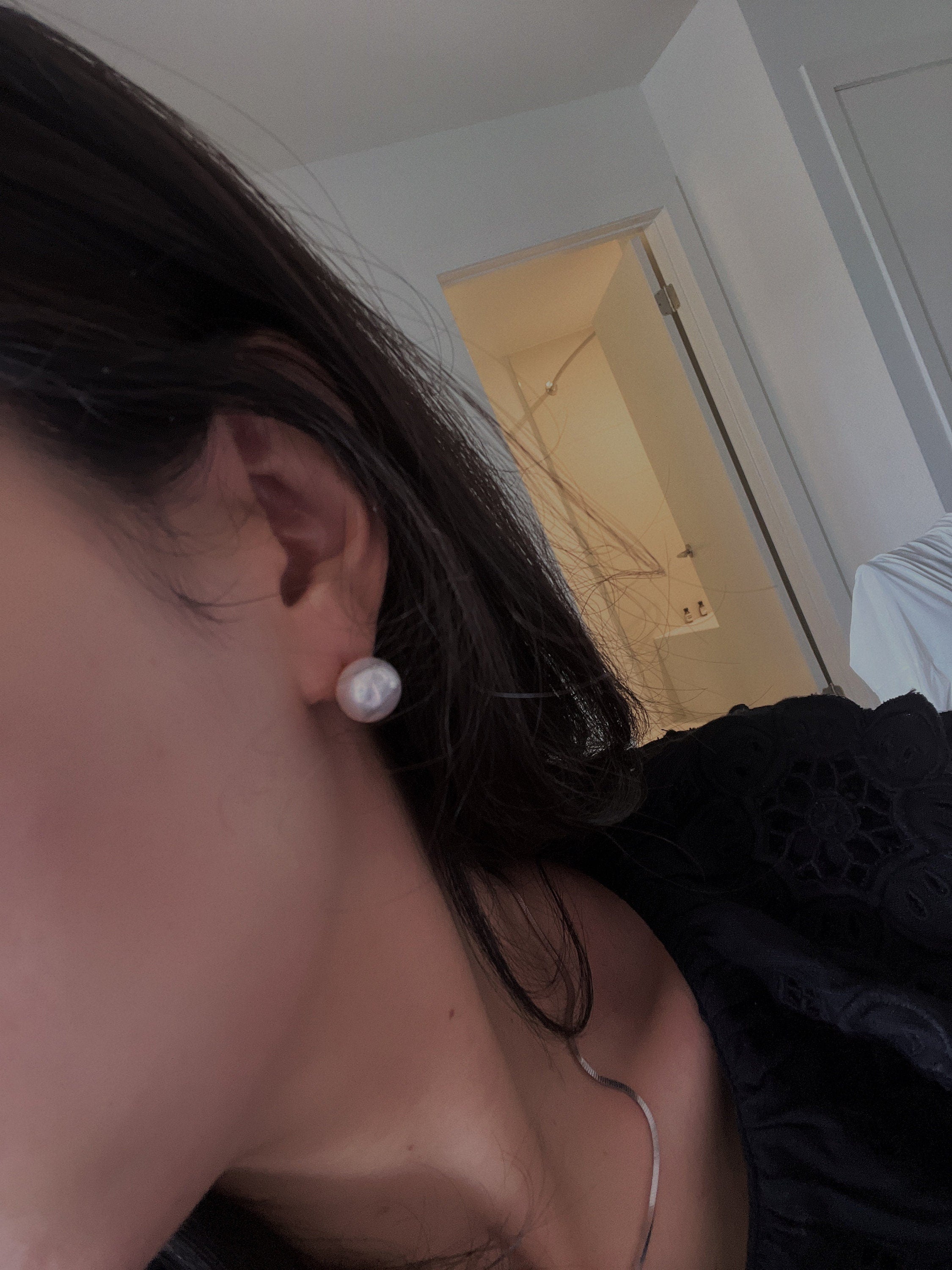 Large white pearl stud earring on a woman's ear.