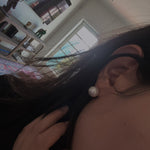 A person wears a single large white pearl stud earring.