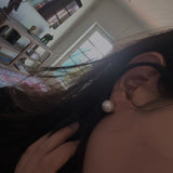 A person wears a single large white pearl stud earring.