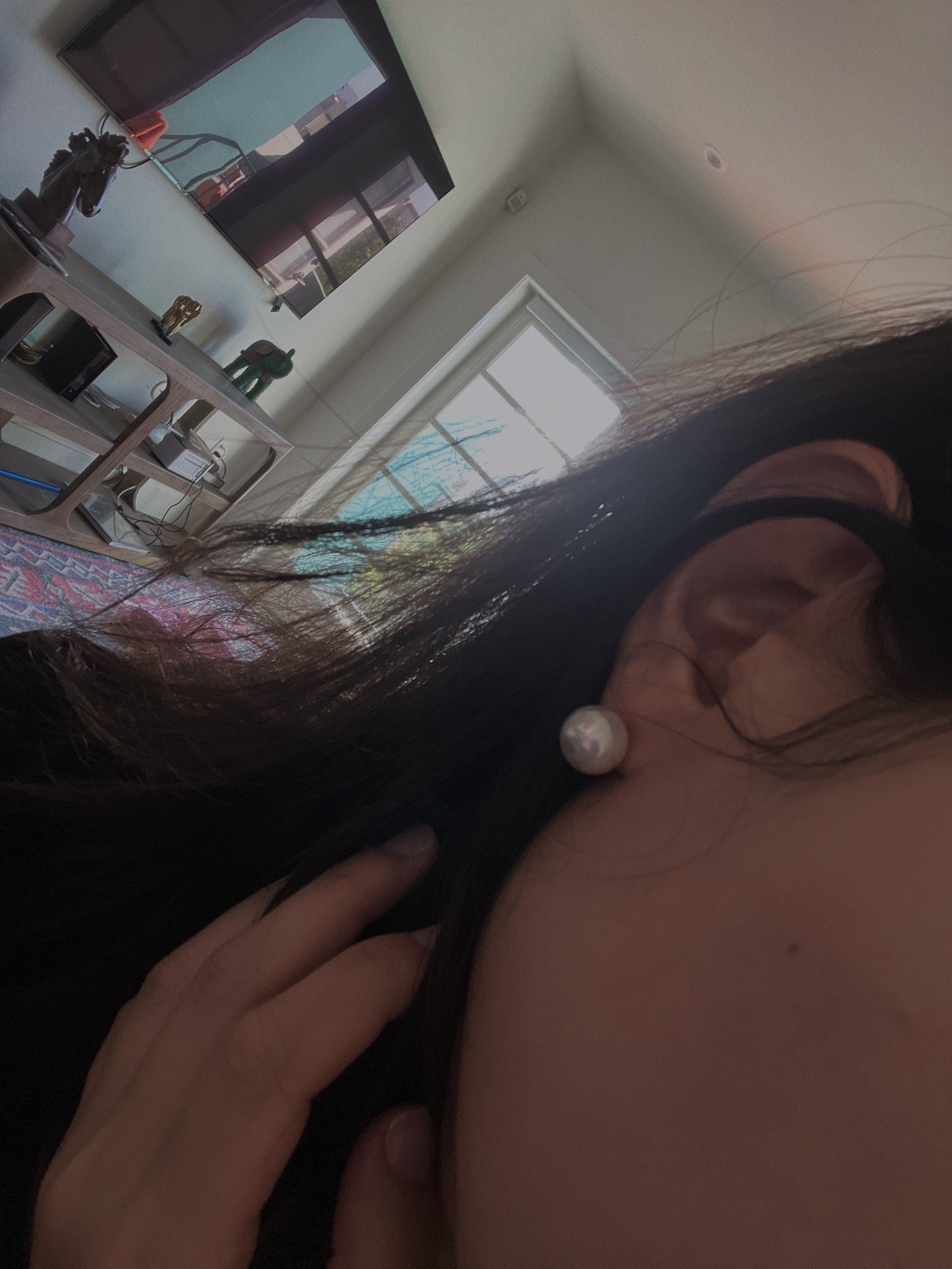 A person wears a single large white pearl stud earring.