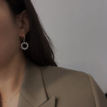 Gold-plated hoop earrings with a dangling circular ring of freshwater pearls.