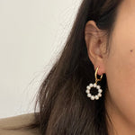 A close-up of a woman wearing a gold hoop earring with a dangling pearl ring.