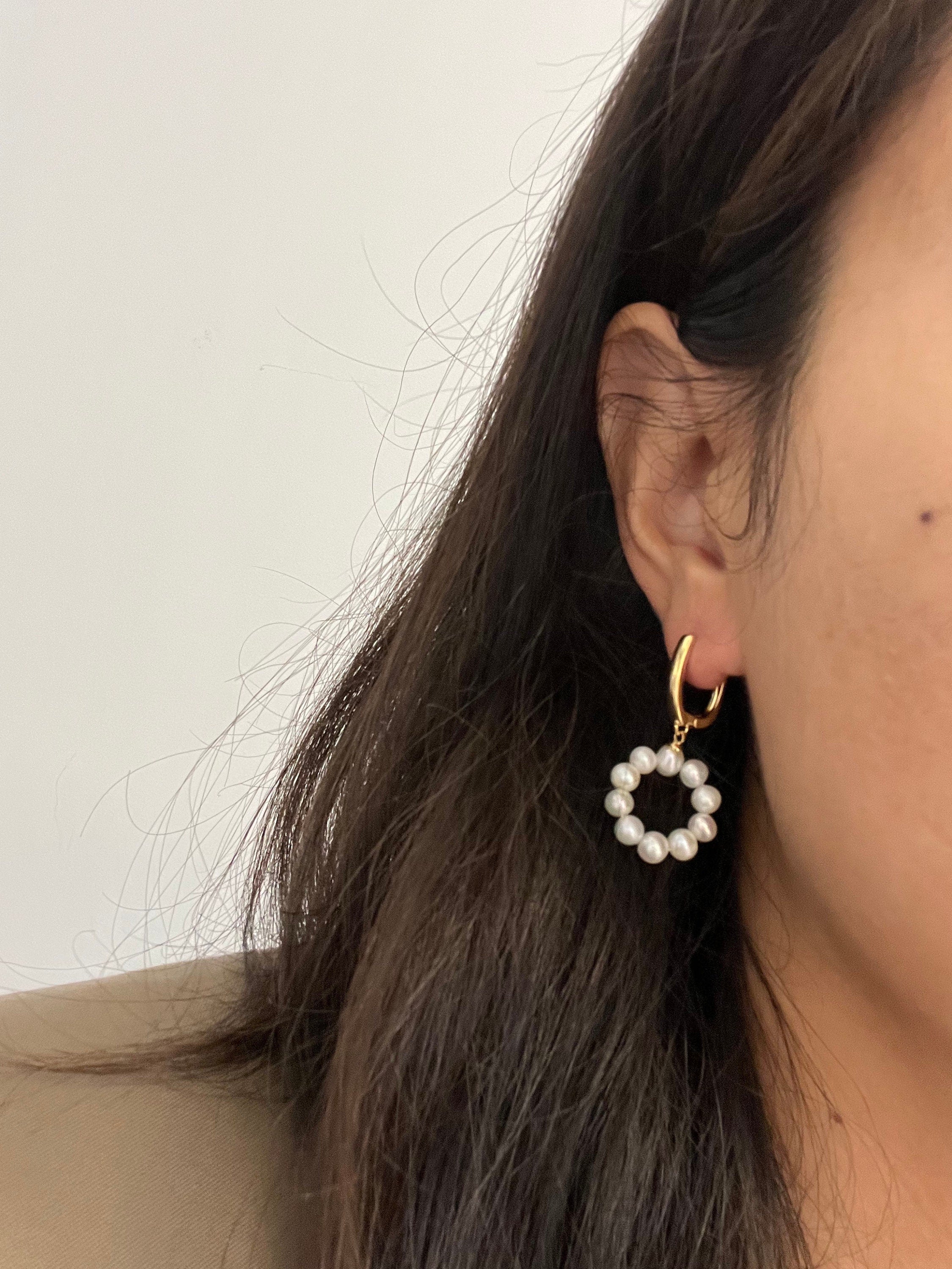A close-up of a woman wearing a gold hoop earring with a dangling pearl ring.