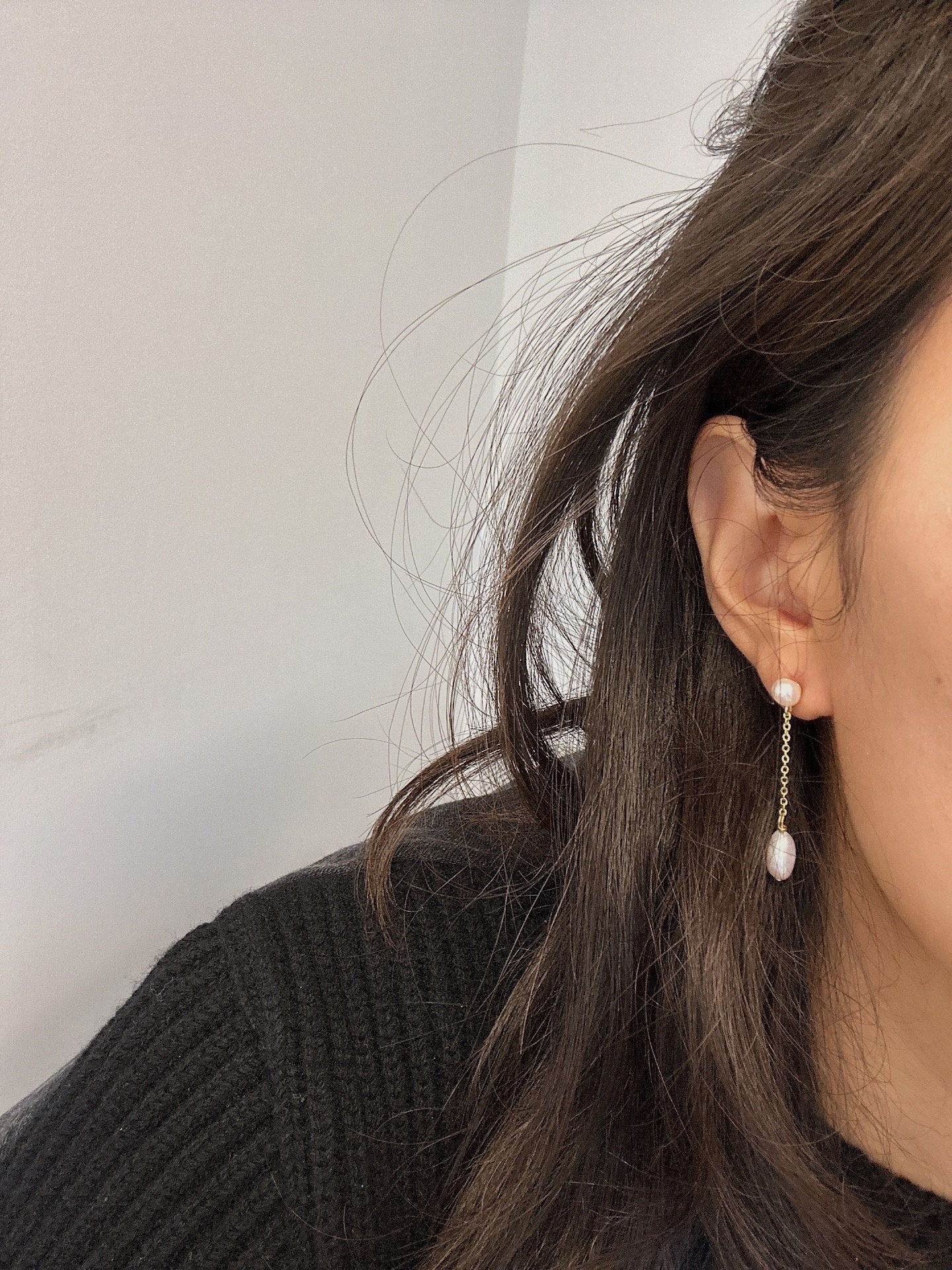 Freshwater pearl drop chain dangling earrings on a person's ear.