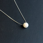 A dainty freshwater pearl pendant necklace with a silver chain on a dark background.