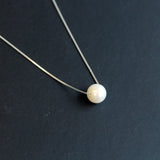 A dainty freshwater pearl pendant necklace with a silver chain on a dark background.