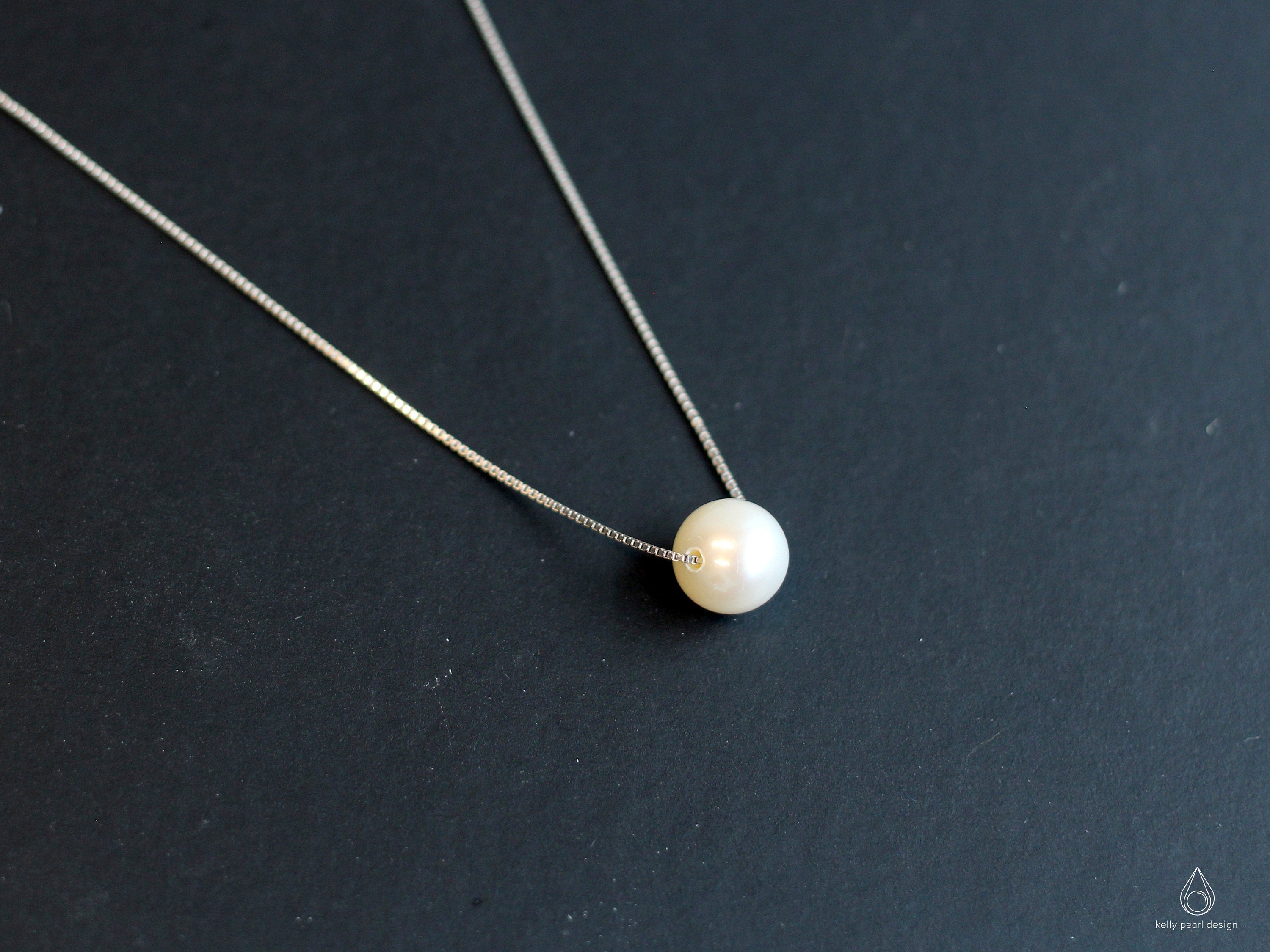 A dainty freshwater pearl pendant necklace with a silver chain on a dark background.