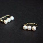 Two gold-plated freshwater pearl earrings, each with three pearls, are displayed on a black surface.