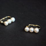 Two gold-plated freshwater pearl earrings, each with three pearls, are displayed on a black surface.