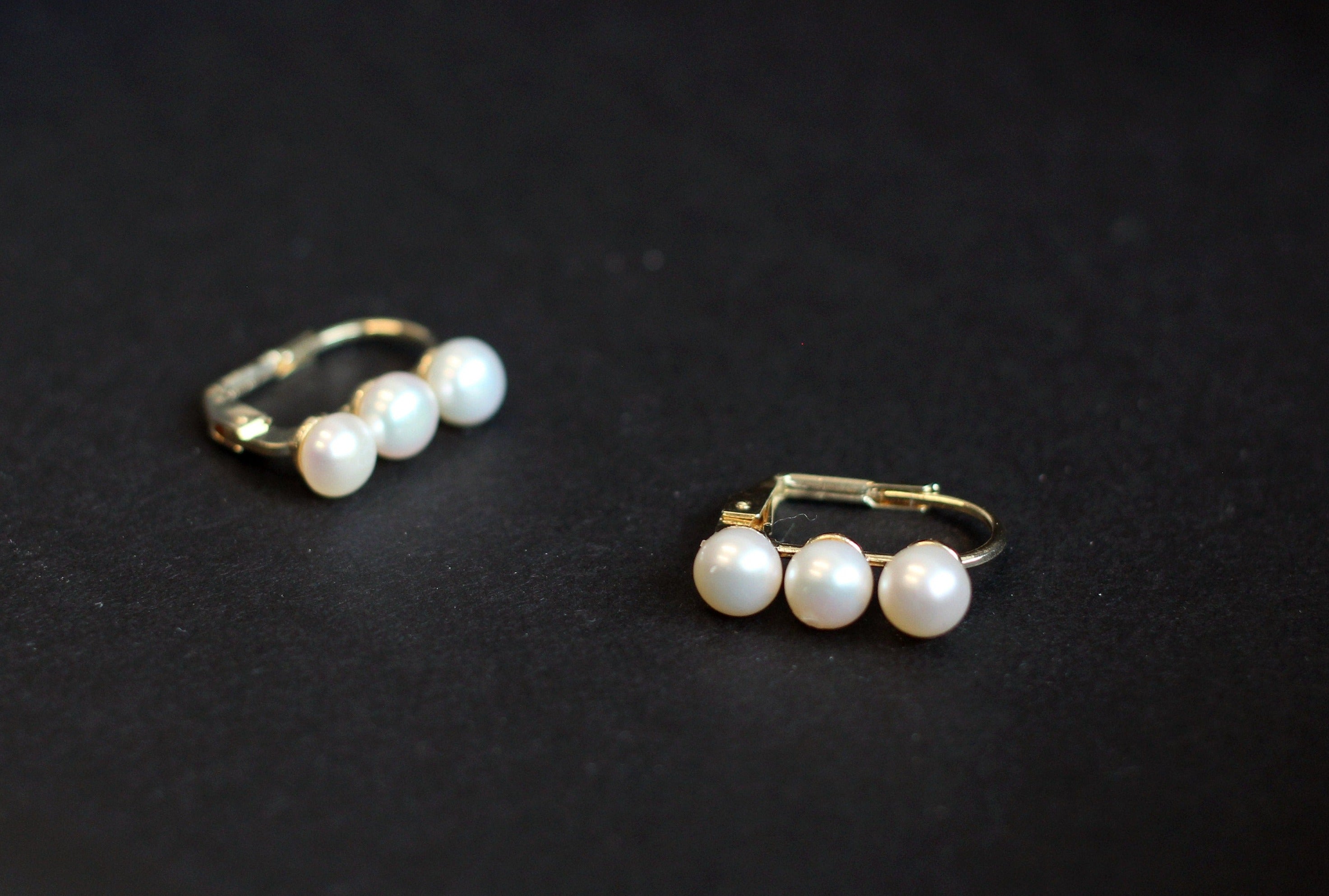 Two gold-plated freshwater pearl earrings, each with three pearls, are displayed on a black surface.