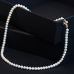 A white freshwater pearl necklace with an 18K gold flower-shaped clasp.