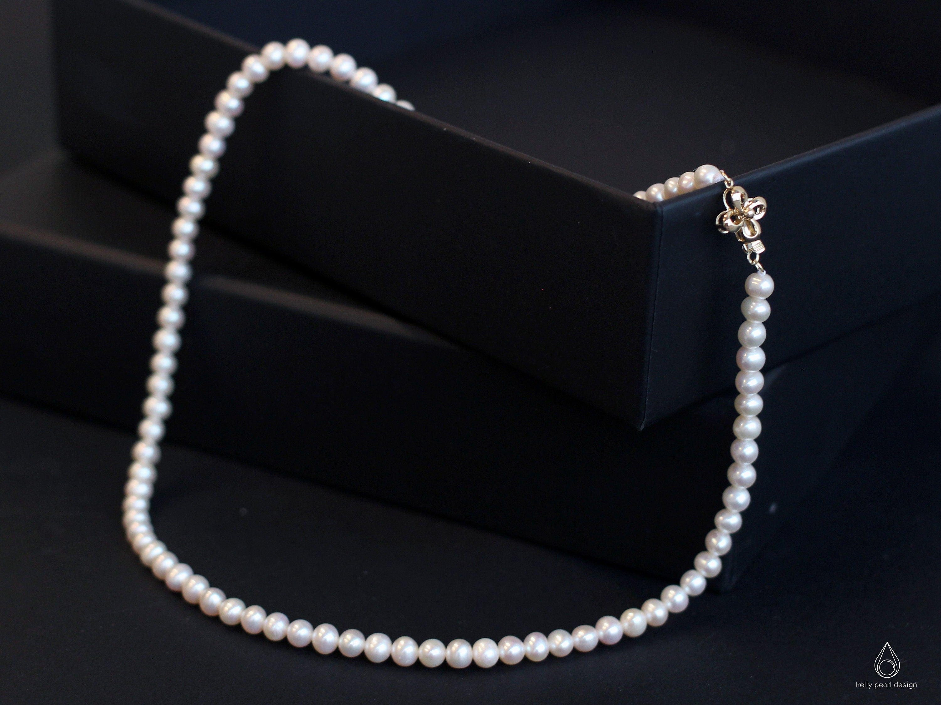 A white freshwater pearl necklace with an 18K gold flower-shaped clasp.