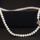 Freshwater pearl necklace with an 18K gold flower-shaped clasp on a black surface.