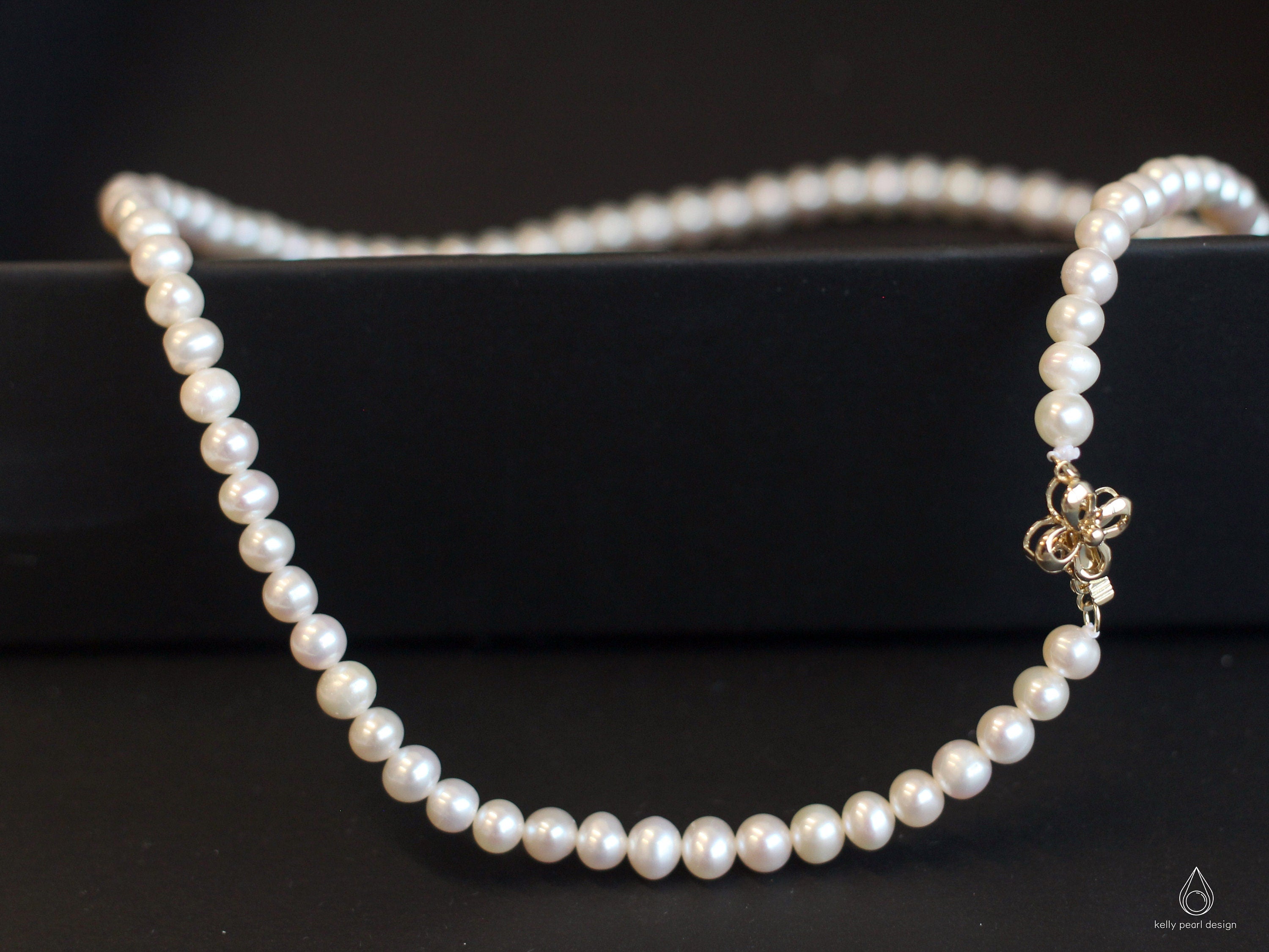 Freshwater pearl necklace with an 18K gold flower-shaped clasp on a black surface.