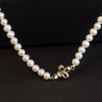 A white freshwater pearl necklace with an 18K gold bow-shaped clasp.
